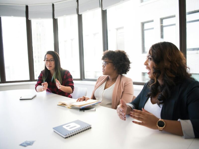 Three Woman Talking Near White Wooden Table Inside Room